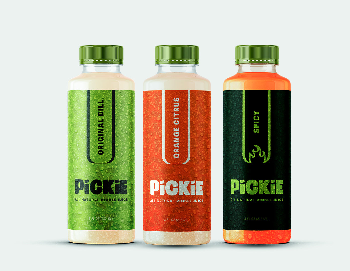 Three PiCKiE pickle juice bottles side by side — Original Dill on the left, Orange Citrus in the middle, and Spicy on the right — showcasing the full pickle juice flavor variety made with real ingredients.