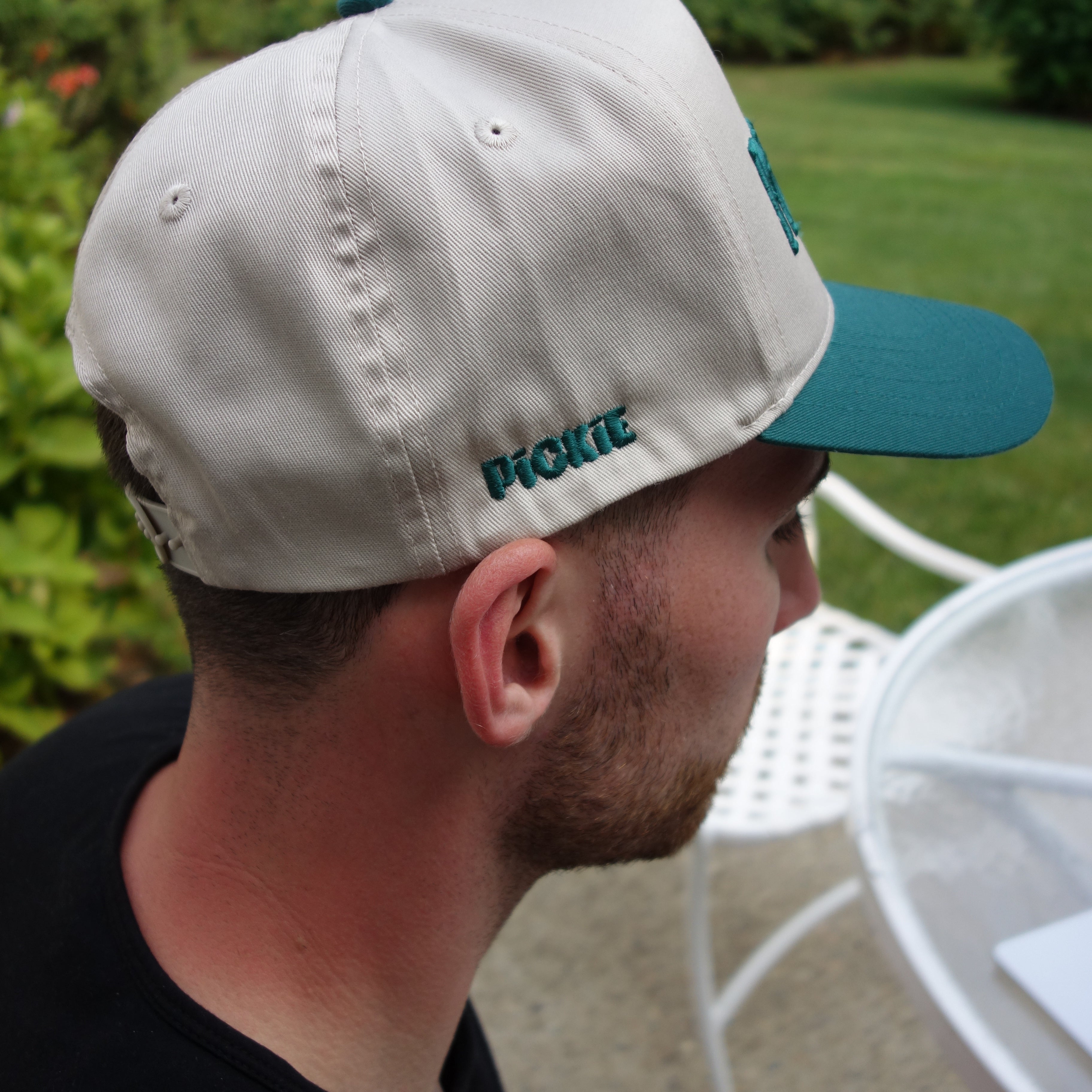 Person wearing a beige cap with a blue bill, looking downwards.