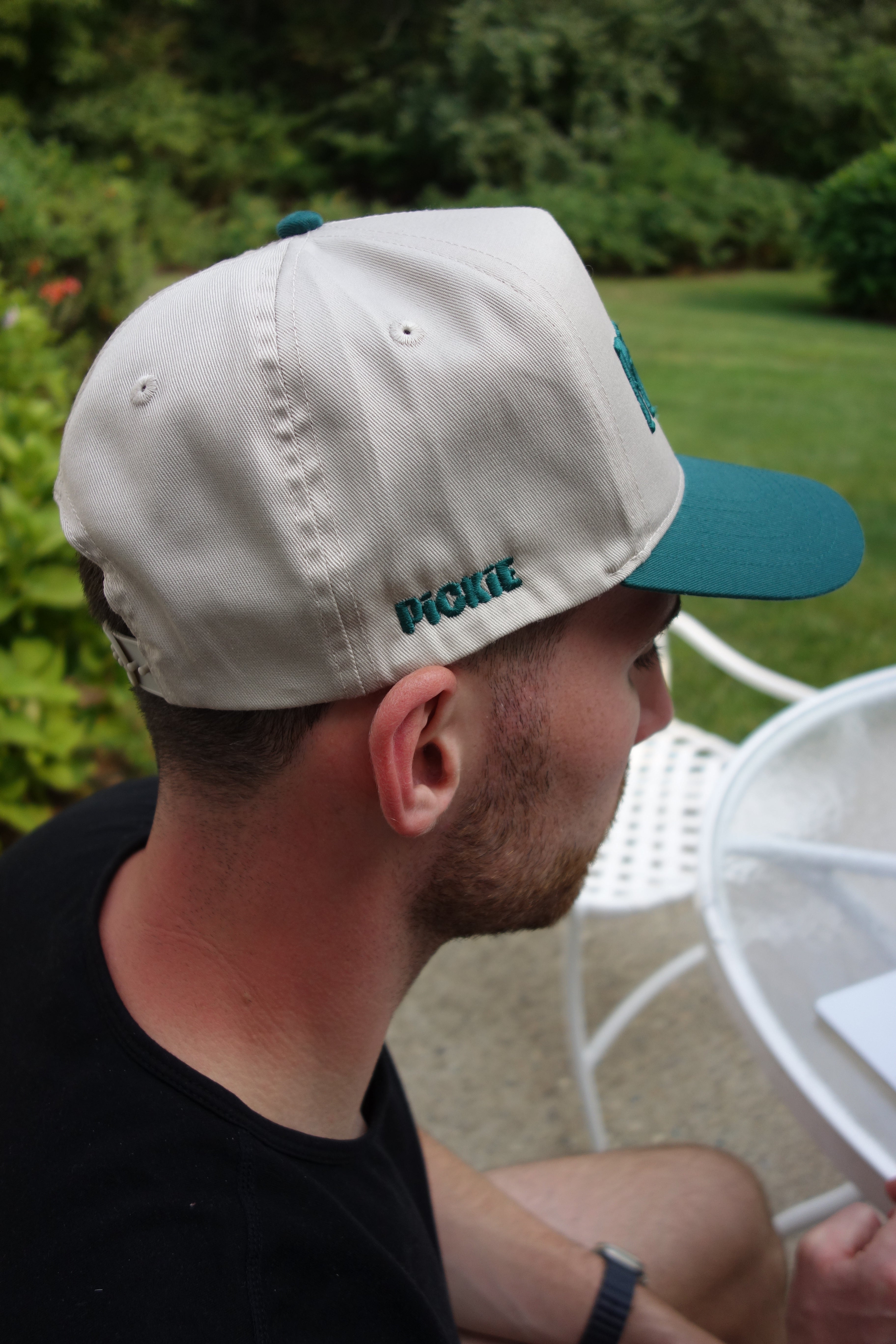Person wearing a beige cap with a blue bill, looking downwards.